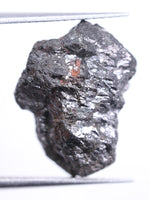Raw diamond held by tweezers on a white background
