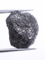 Raw diamond held between tweezers on a white background