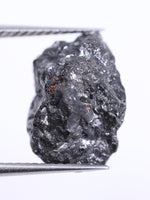 Raw diamond held by tweezers on a white background