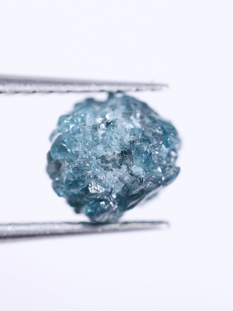 Blue diamond held between tweezers on a white background