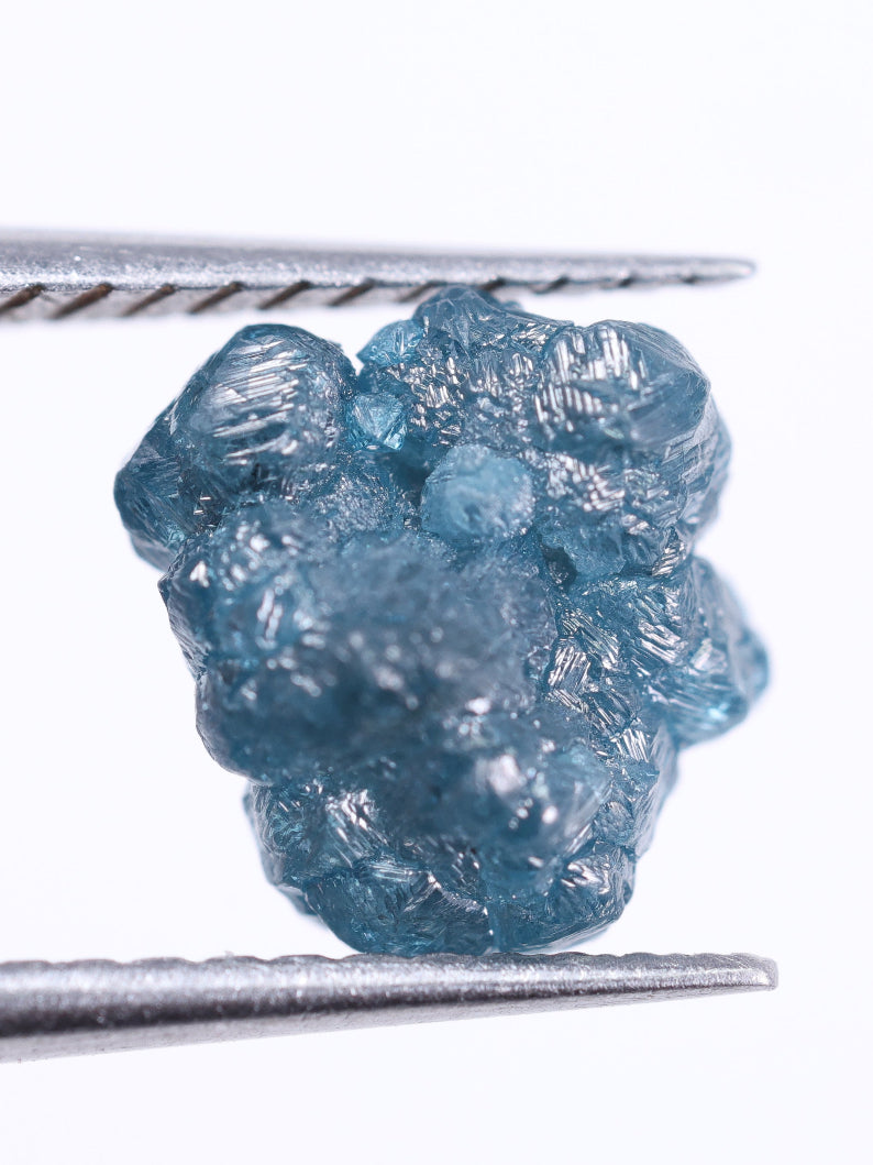 Raw blue diamond held between tweezers on a white background