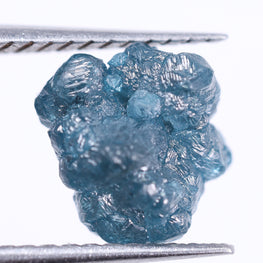 Raw blue diamond held between tweezers on a white background