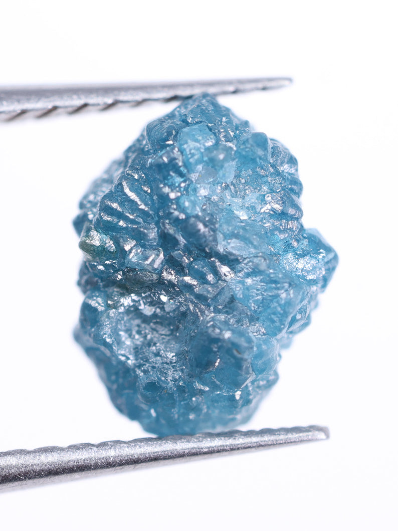 Raw blue diamond held by tweezers on a white background