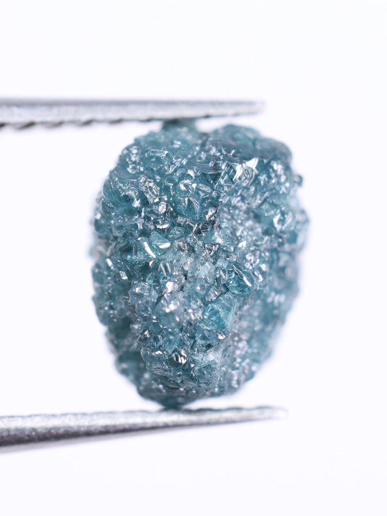 Raw blue diamond held by tweezers on a white background