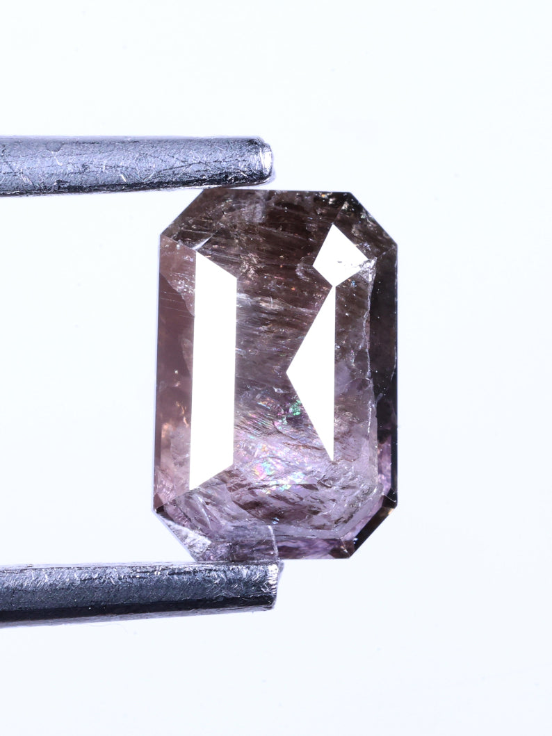 emerald shape brownish purple held between tweezers on a white background