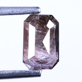 emerald shape brownish purple held between tweezers on a white background