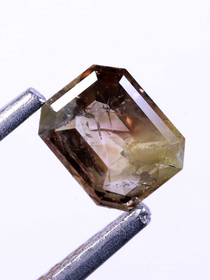 emerald natural diamond held between two tweezers on a white background