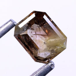 emerald natural diamond held between two tweezers on a white background
