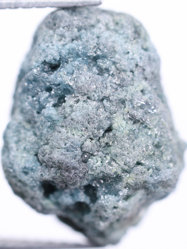 Raw blue stone held by tweezers on a white background