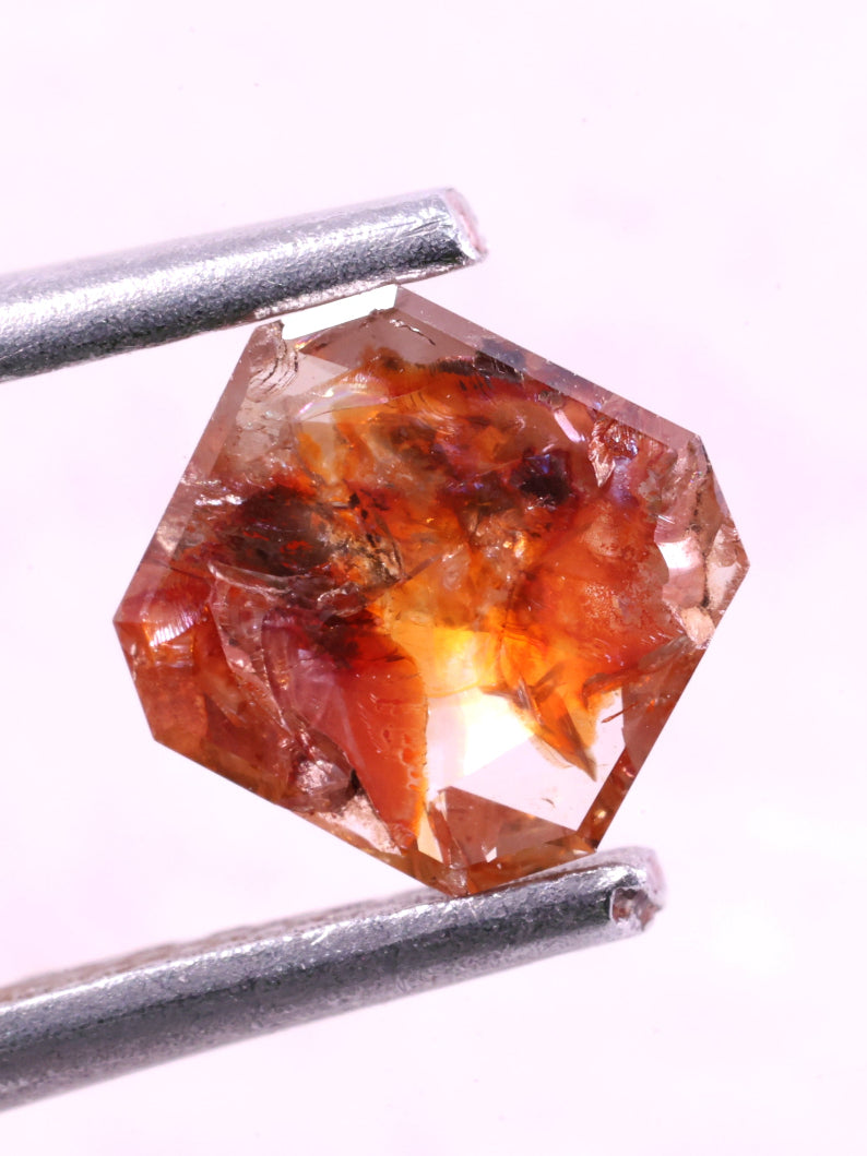 red natural diamond held by tweezers on a white background