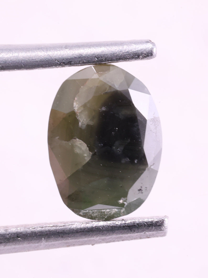 Green diamond held between tweezers on a white background