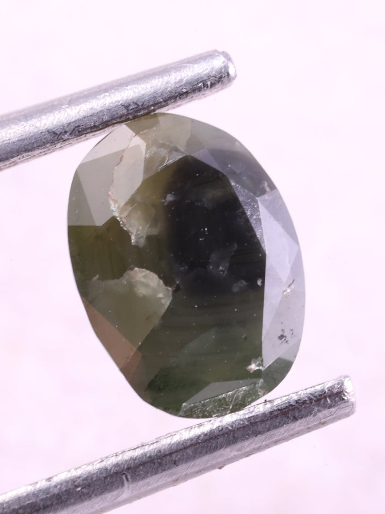 Green diamond held by tweezers on a white background