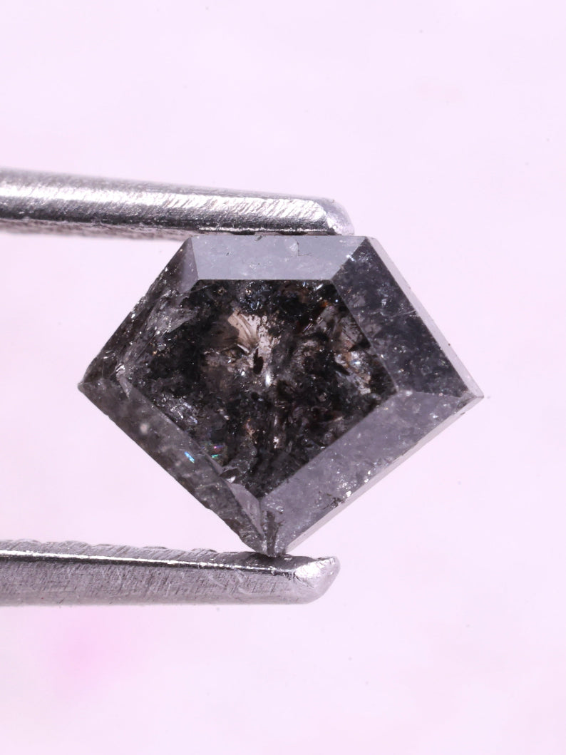 Shield diamond held by tweezers on a light pink background