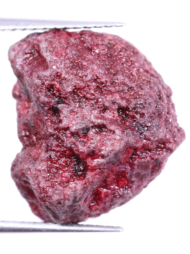 Raw red diamond held by tweezers on a white background