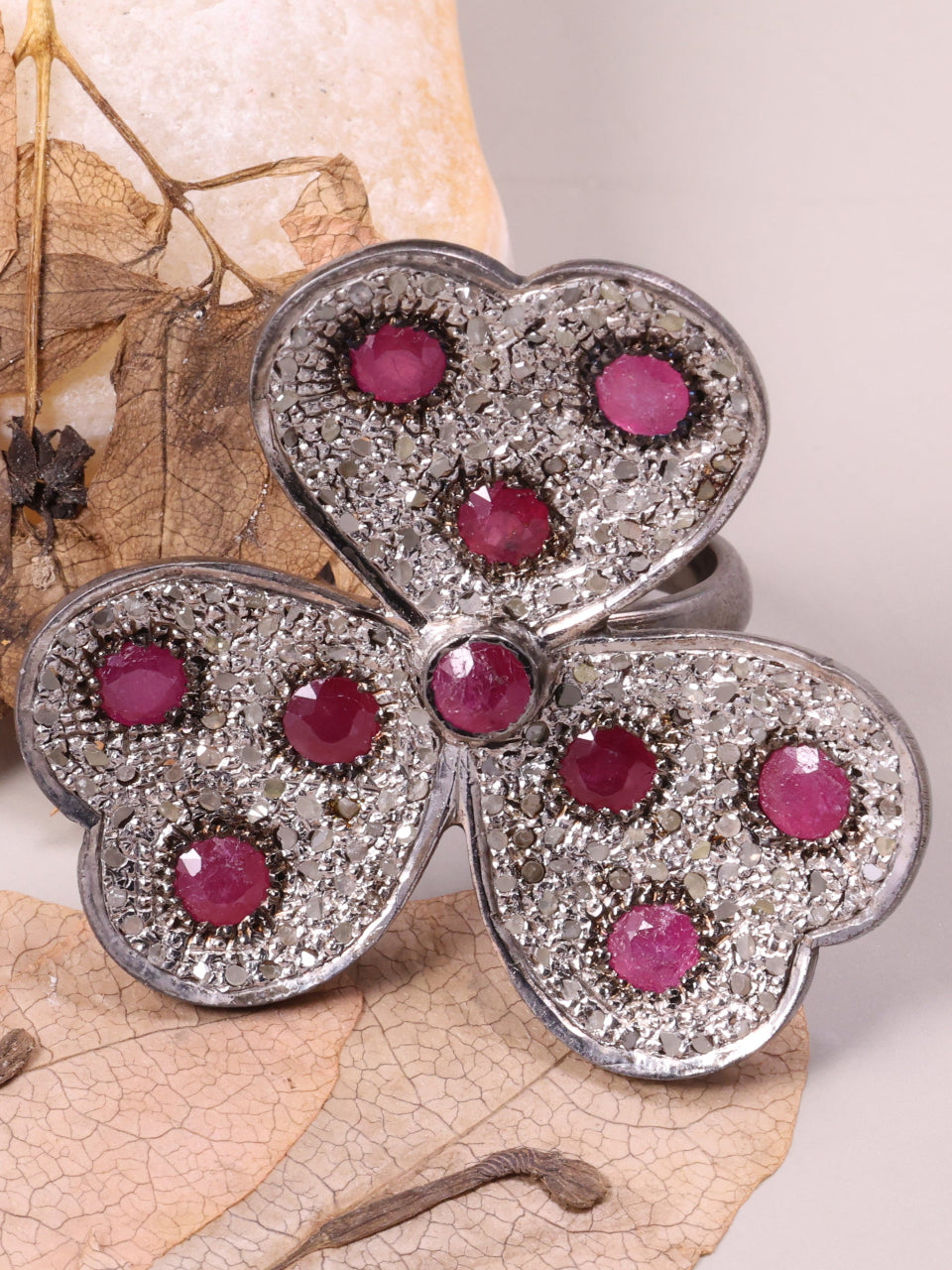 Butterfly-shaped jewelry piece with pink stones on a leaf background