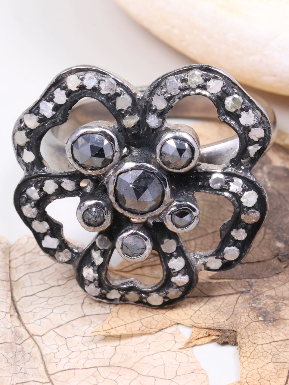 Silver flower-shaped brooch with gemstones on a leafy background