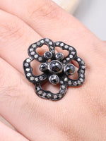 Floral silver ring with black stones on a hand against a neutral background
