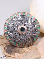 Decorative button with gemstones on a white surface with leaves