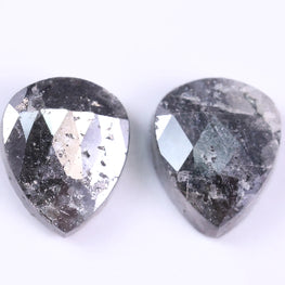 Two teardrop-shaped diamond with a dark, textured surface on a white background