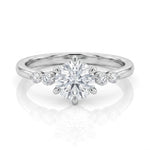 A silver solitaire engagement ring with a round-cut center stone and smaller accent stones on the band, shown on a clean white background with a soft reflection.
