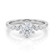 A silver solitaire engagement ring with a round-cut center stone and smaller accent stones on the band, shown on a clean white background with a soft reflection.