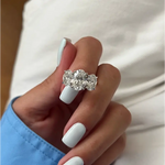 Three-stone oval diamond engagement ring in white gold on a woman’s hand with light blue manicure