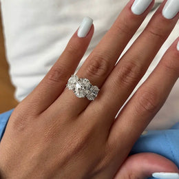 Three-stone oval diamond engagement ring in white gold on a woman’s hand with light blue manicure