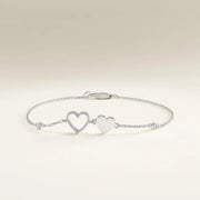 Silver bracelet with two heart charms on a light beige background