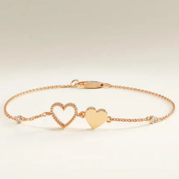 Gold bracelet with heart charms on a wrist against a neutral background