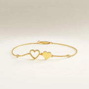 Gold bracelet with heart charms on a wrist against a neutral background