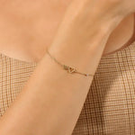 Gold bracelet with heart charms on a wrist against a neutral background