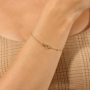 Gold bracelet with heart charms on a wrist against a neutral background