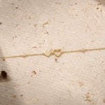 Gold bracelet with heart charms on a wrist against a neutral background