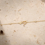 Gold bracelet with heart charms on a wrist against a neutral background