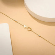 Gold bracelet with heart charms on a wrist against a neutral background